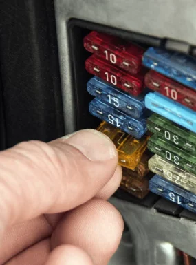 Technician removing a blown fuse from a car’s fuse box