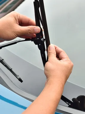 Technician replacing windshield wipers on car windshield